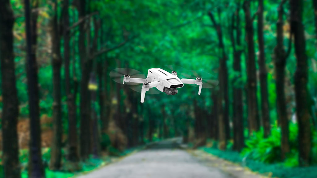 Dron pequeño blanco volando sobre un camino de un parque muy frondoso y verde